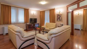 Ein Wohnzimmer mit einer Couch, Sesseln, einem Couchtisch und einem Fernseher.