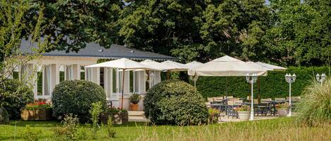 Ein Garten mit Sitzgelegenheiten im Freien und ein Gebäude mit weißer Fassade und Rundbogenfenstern.