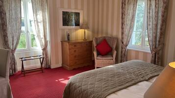 A bedroom with a bed, a chair, a dresser, and a window with curtains.