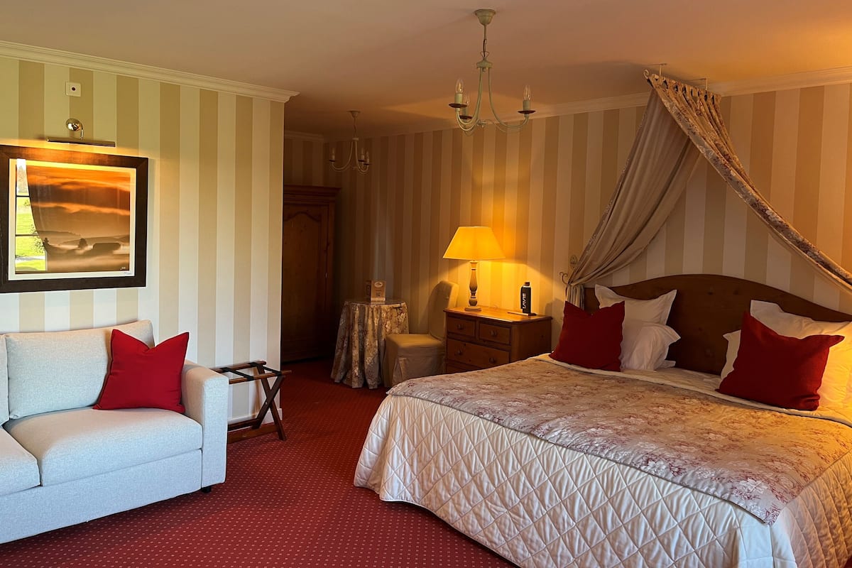 Una habitación de hotel con cama, sofá, mesita de noche, lámpara y un cuadro en la pared.