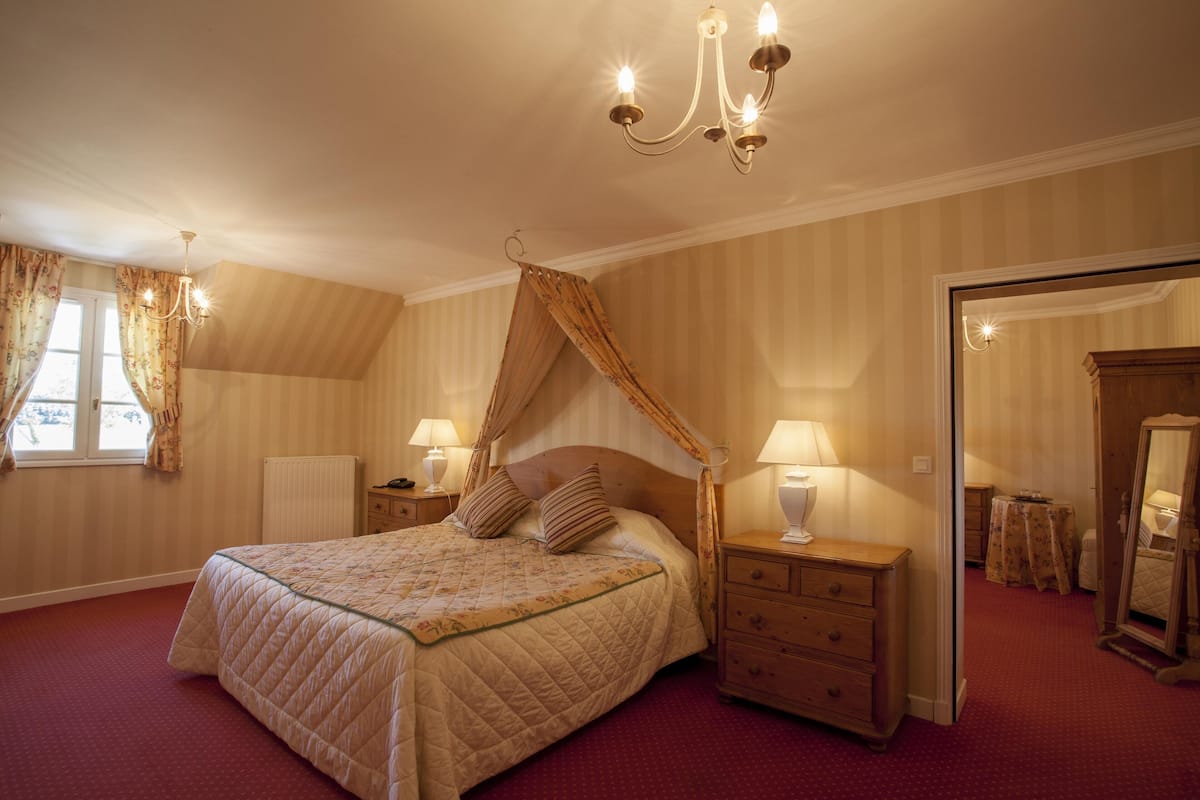 Un dormitorio con una cama grande, dos mesitas de noche con lámparas, una mesita de madera, un espejo y una ventana con cortinas.
