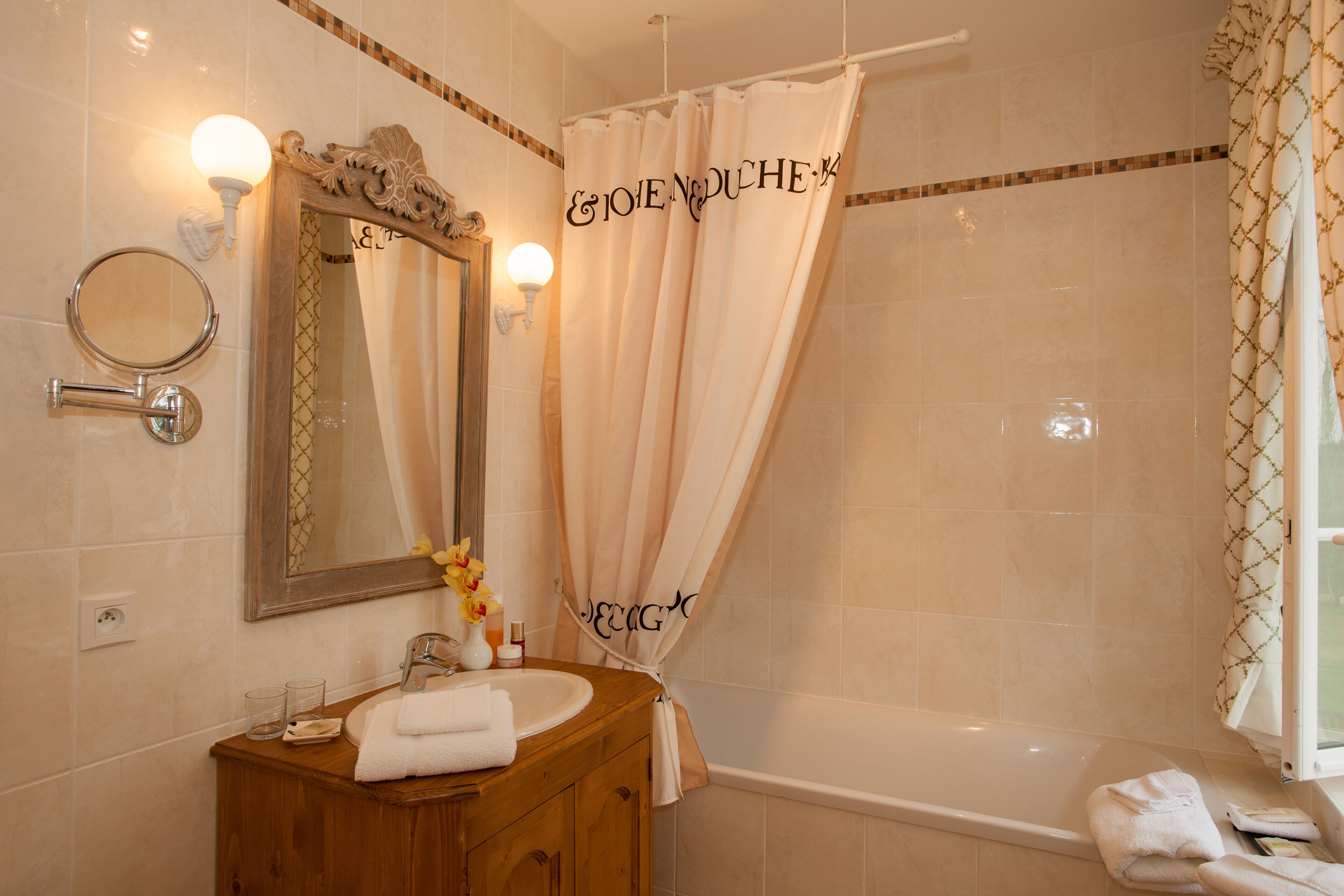 Un baño con tocador de madera, un espejo redondo, lavamanos, toalla, cortina de ducha con texto y bañera.