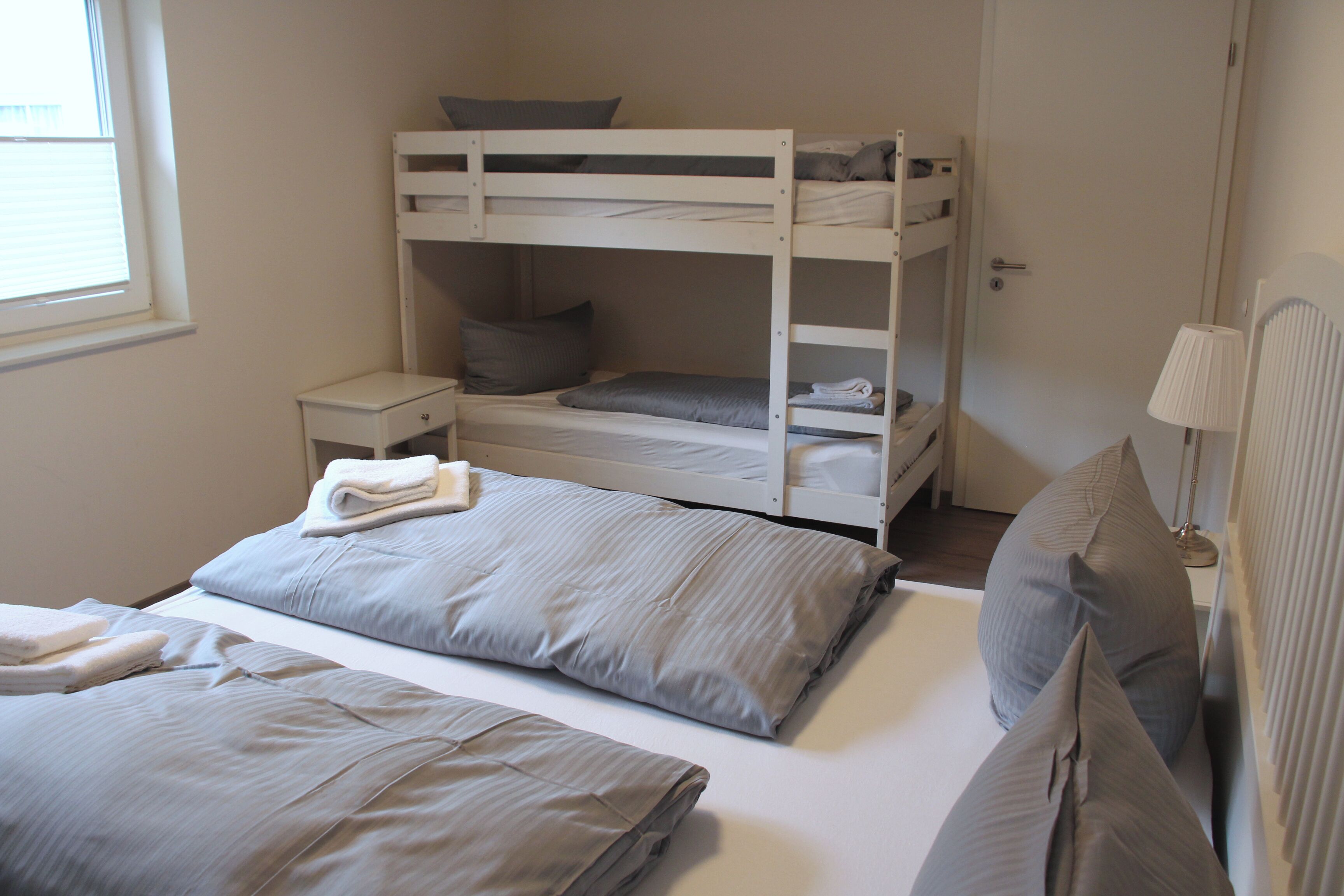 A bunk bed room with a small bedside table, a lamp, and a window.
