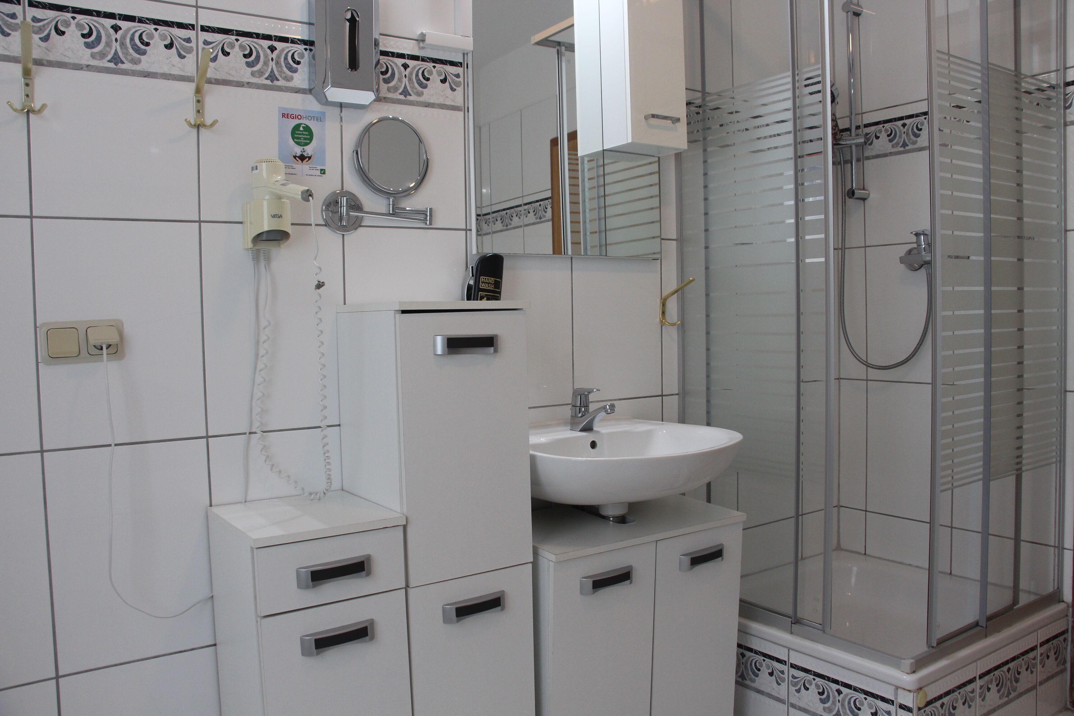 A bathroom with a white sink, a mirror, a shower enclosure, and a telephone.
