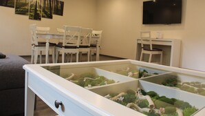 Un salon avec une table basse en verre, des chaises blanches, un téléviseur à écran plat et des œuvres d’art accrochées au mur.
