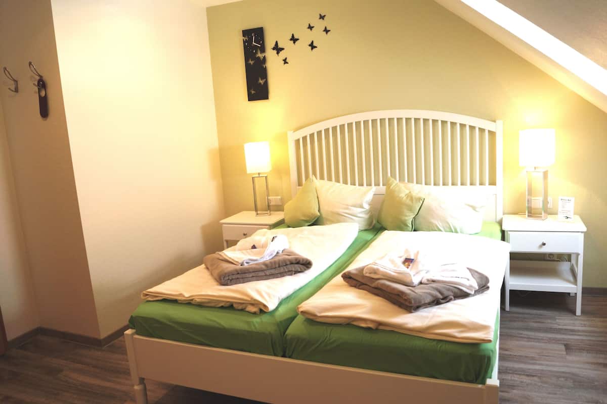 A neatly made double bed with green bedding, two bedside tables with lamps, and a wall clock.