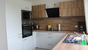 Une cuisine moderne avec des meubles blancs et en bois, des appareils en acier inoxydable, un four à micro-ondes et un évier équipé d’un égouttoir.