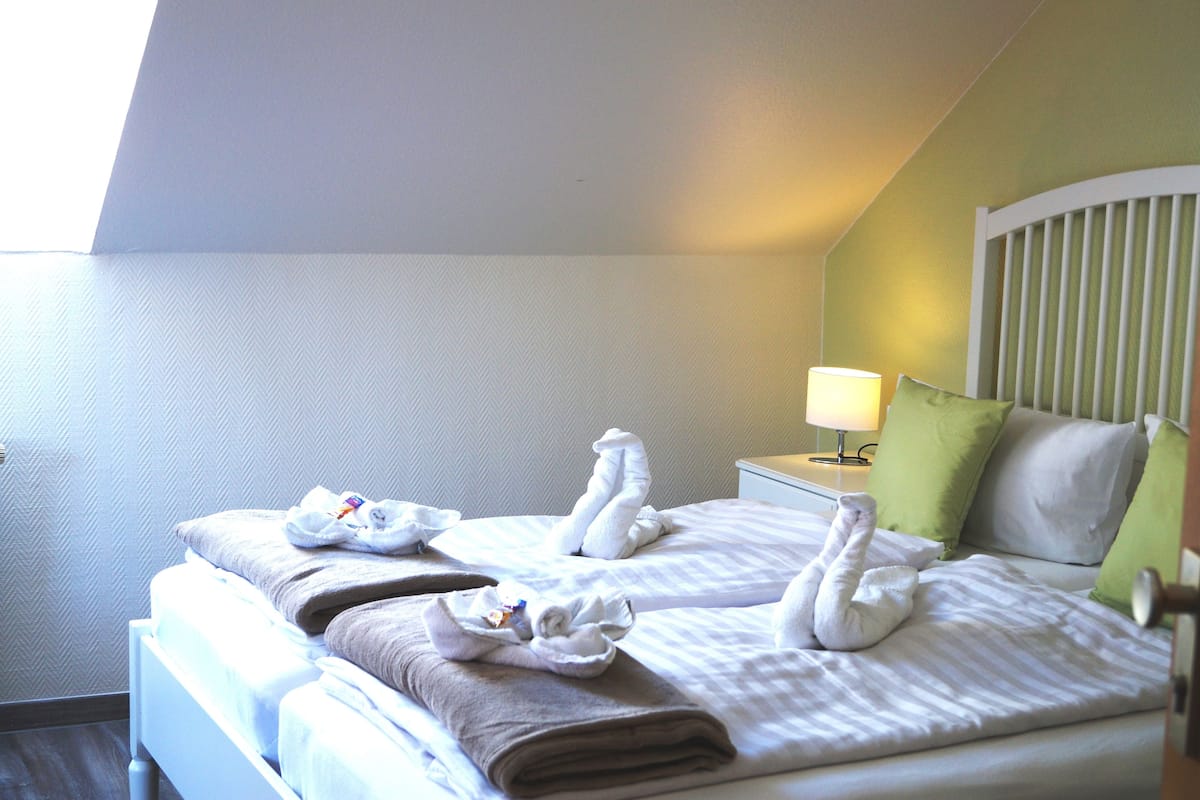 A hotel room with two beds, a nightstand with a lamp, and a green pillow.