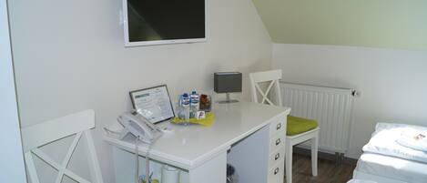 Une petite pièce propre, équipée d’un bureau, d’une chaise et d’un lit. Un téléviseur est fixé au mur, il y a aussi un radiateur et une fenêtre.