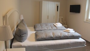 Une chambre à coucher avec un lit, des oreillers, une table de chevet, une lampe, une armoire et un téléviseur.
