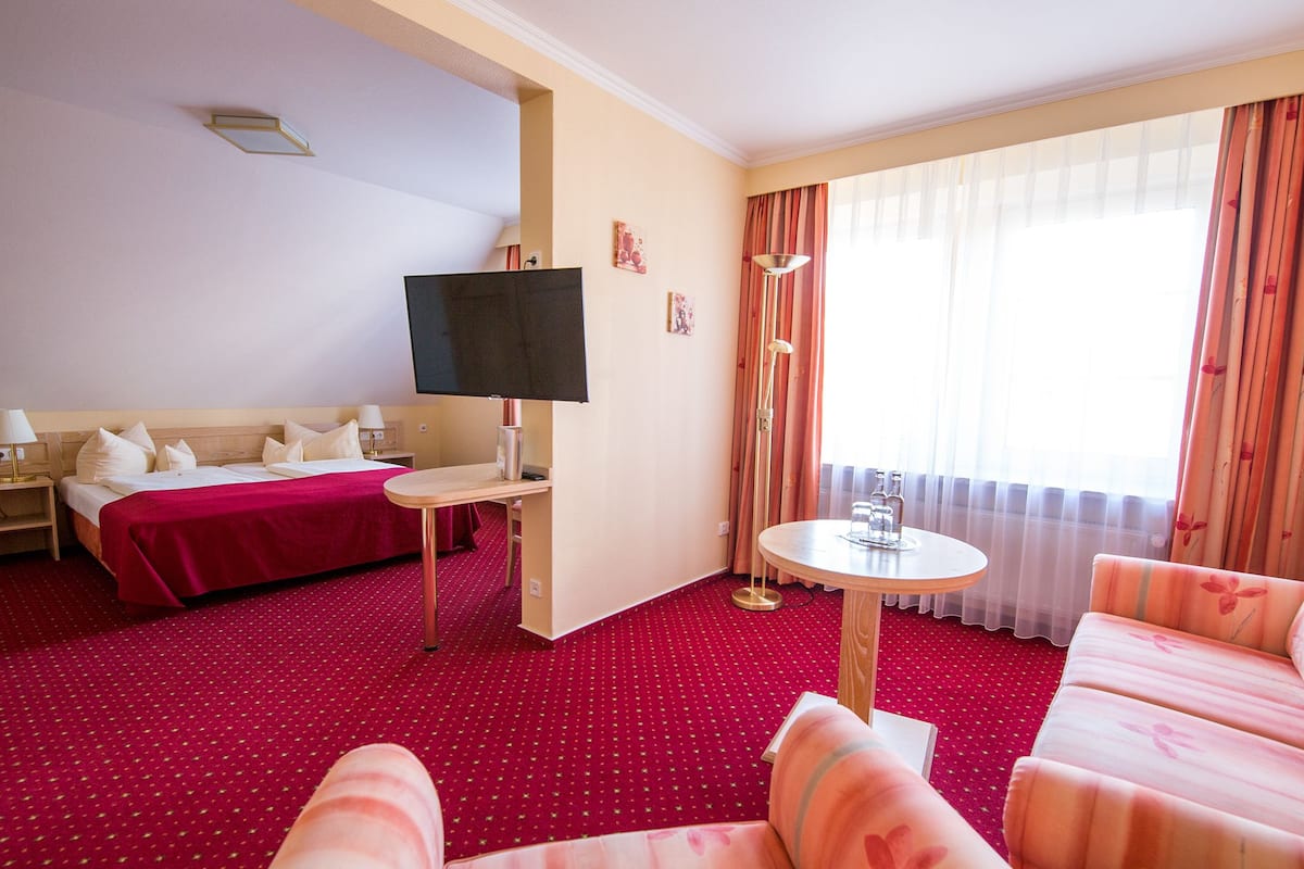 A hotel room with a bed, a TV, a small table, a sofa, and a window with curtains.