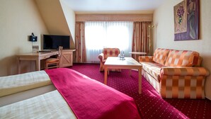 Habitación de hotel con dos camas, un escritorio con ordenador, una silla, un sofá, una mesa de centro y un cuadro en la pared.