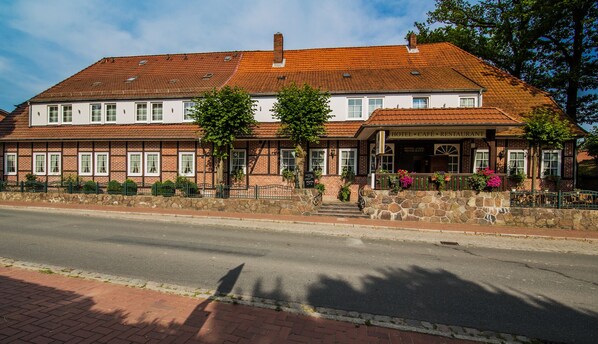 A two-story building with a red-tiled roof, a stone facade, and a sign indicating it is a hotel, cafe, and restaurant. - Hotel Acht Linden (Egestorf)
