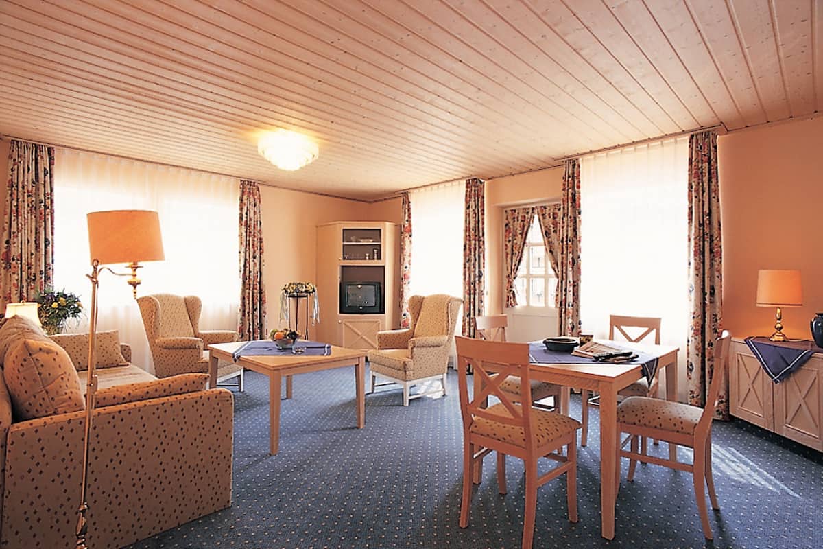 A hotel room with a living area featuring a sofa, armchairs, a dining table, and a TV.