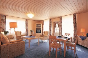 A hotel room with a living area featuring a sofa, armchairs, a dining table, and a TV. - Hotel Acht Linden (Egestorf)