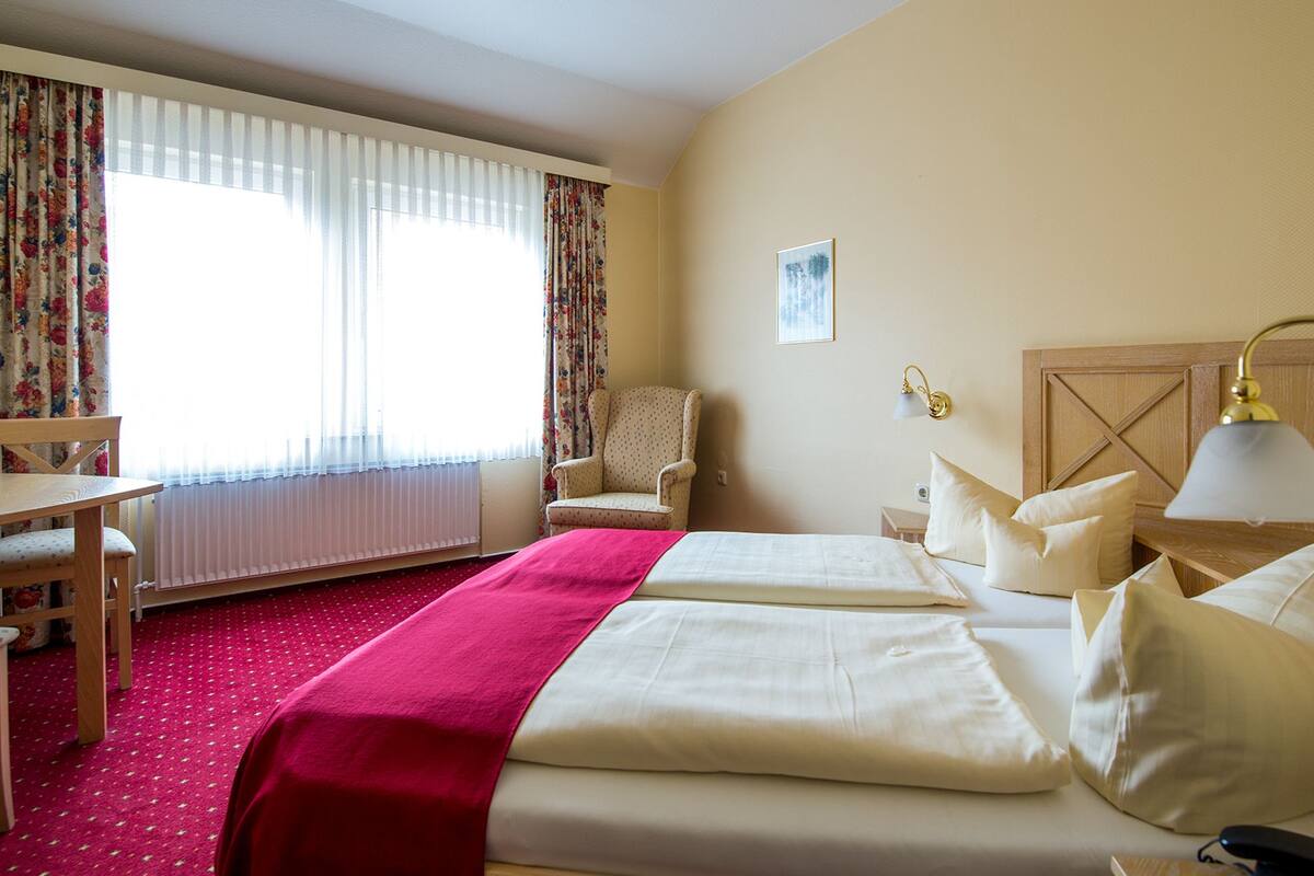 A hotel room with a bed, a chair, a desk, and a lamp.