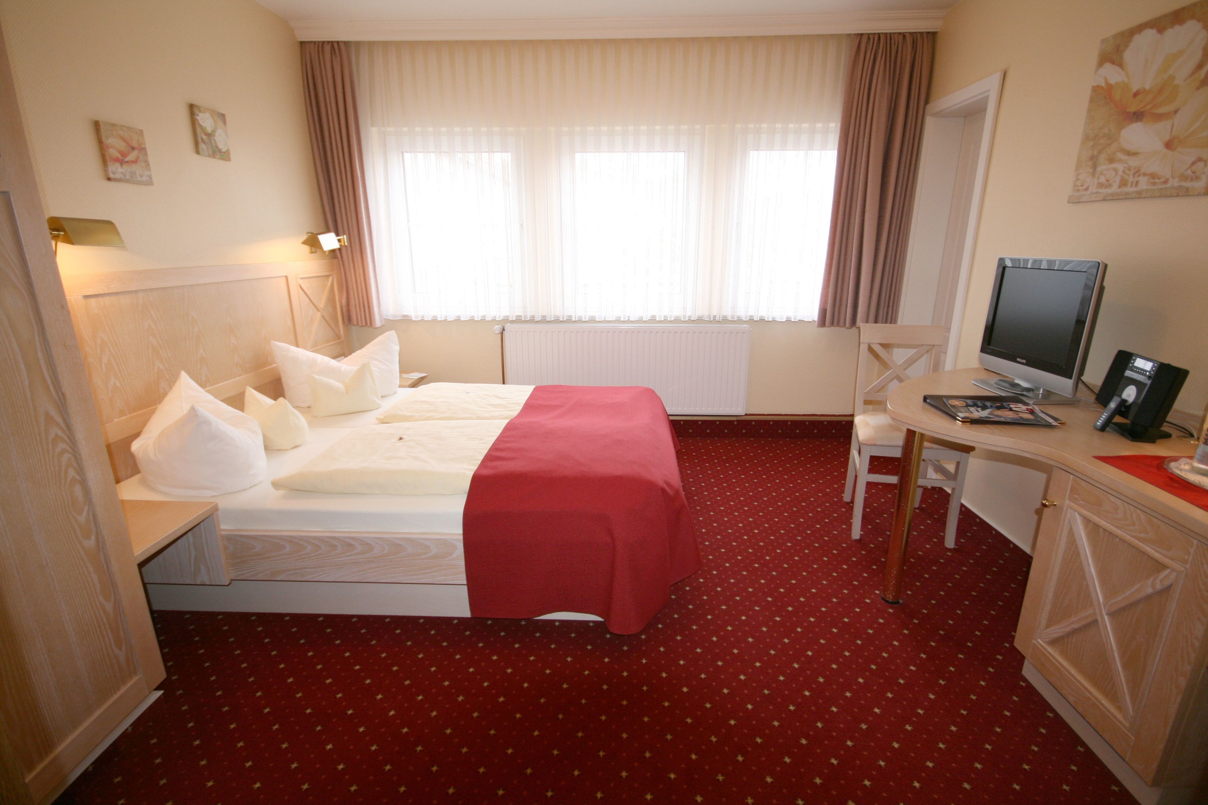 A hotel room with a bed, a desk with a computer, a chair, and a window with curtains.