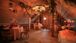 Un interior con paredes de madera, mesas redondas dispuestas para comer y faroles colgantes.
