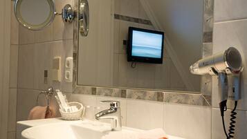 Une salle de bain équipée d’un lavabo, d’un miroir, d’un sèche-cheveux et d’un téléviseur fixé au mur.