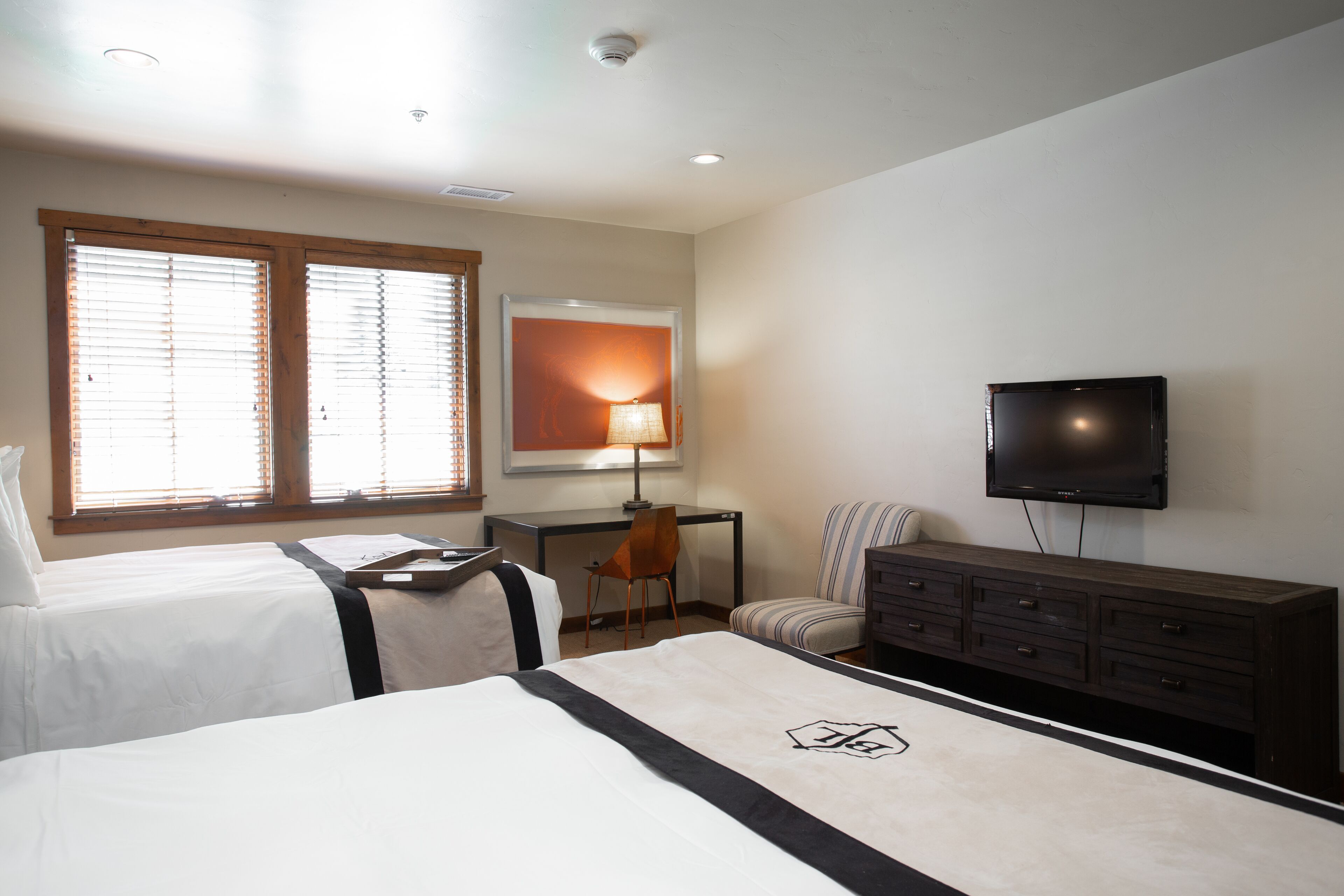 A hotel room with two beds, a desk, a chair, a TV, and a dresser.