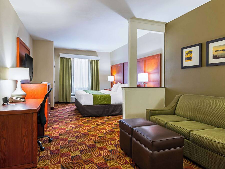 A hotel room with a bed, a green sofa, a desk with a lamp, and a patterned carpet.