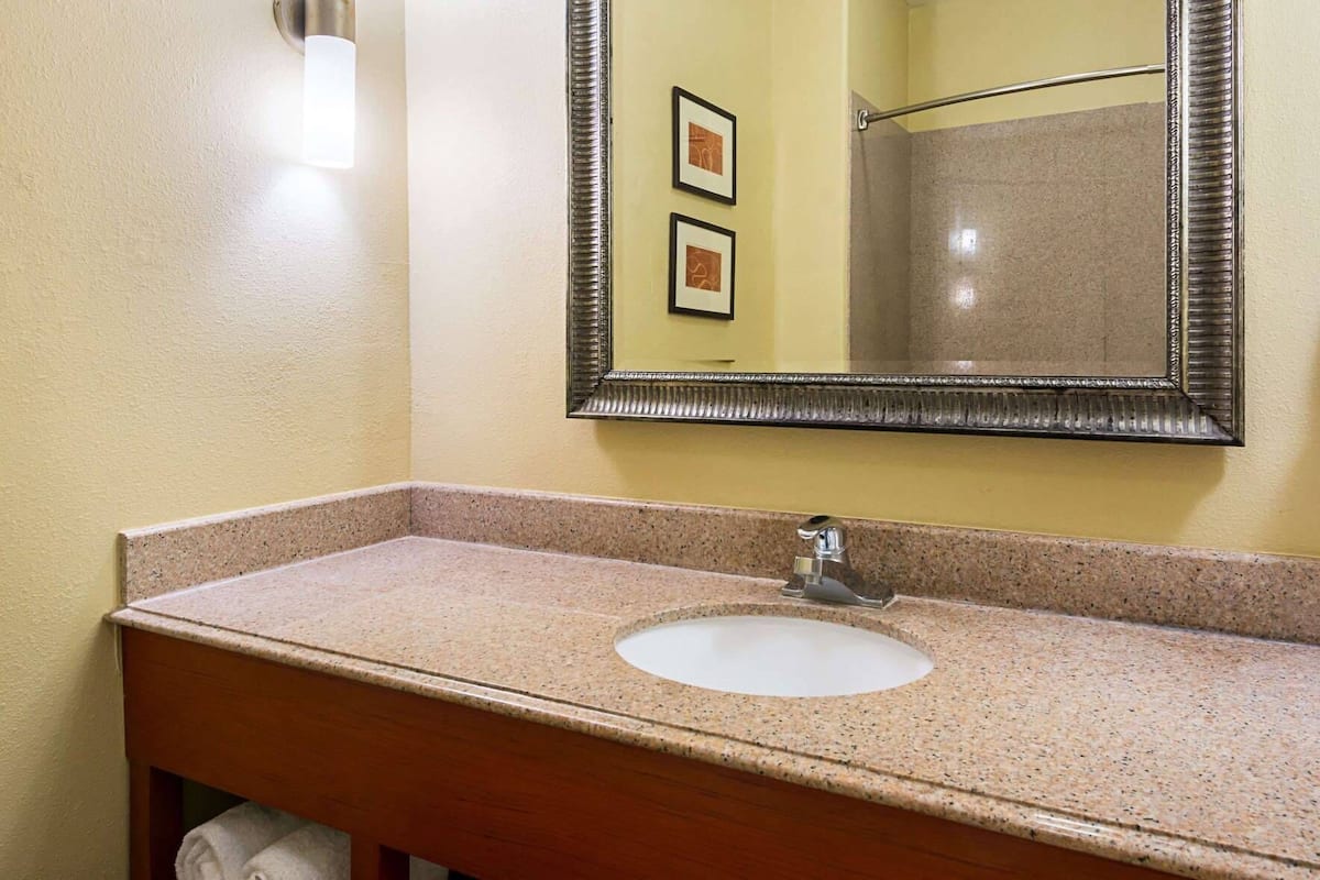 A bathroom with a granite countertop, a white sink, a mirror with a decorative frame, and a towel rack.