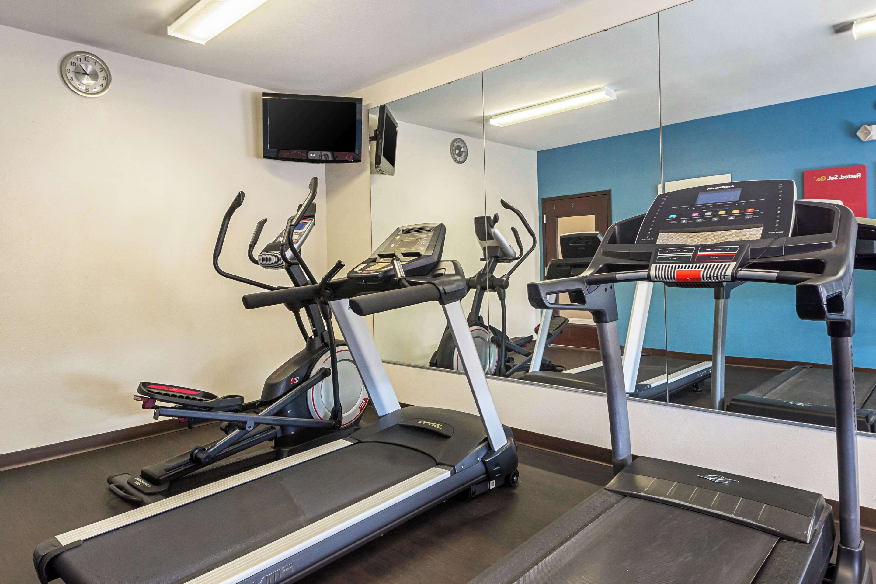 A gym with treadmills, a mirrored wall, a clock, and a TV.