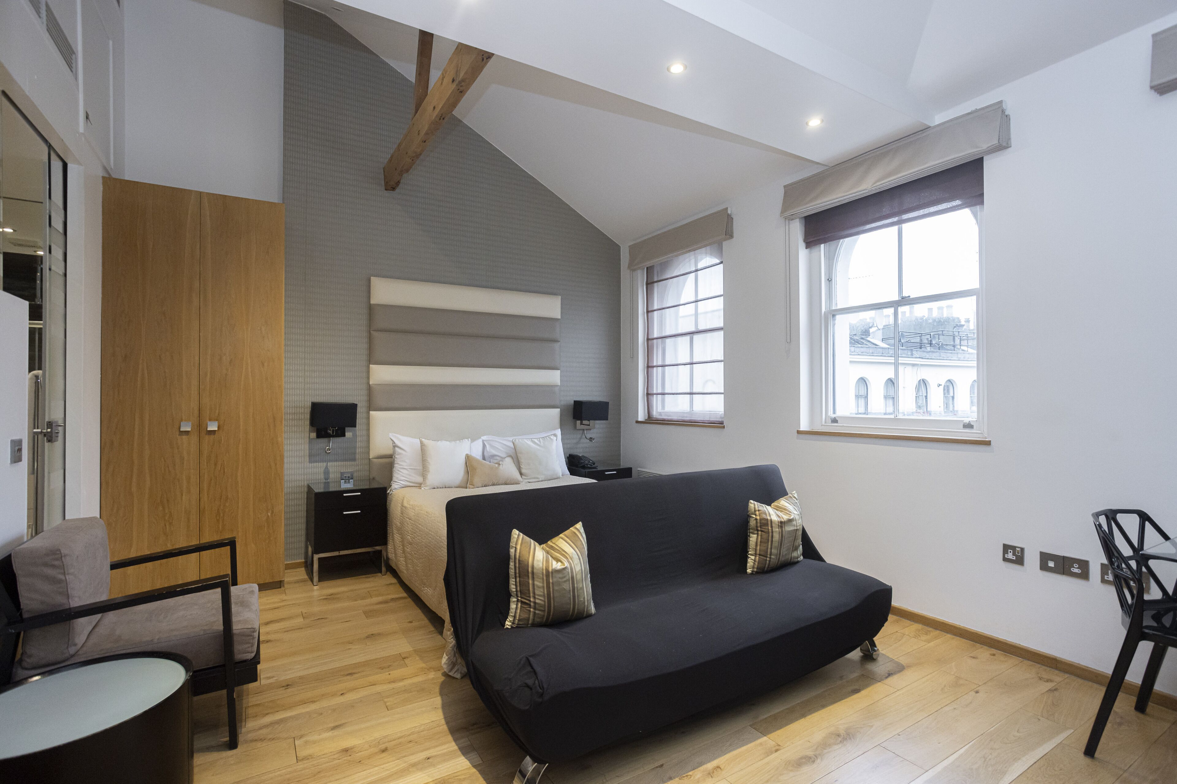 Una camera da letto moderna con un letto, un divano nero, un armadio in legno, un tavolino e una finestra con vista sulla città.