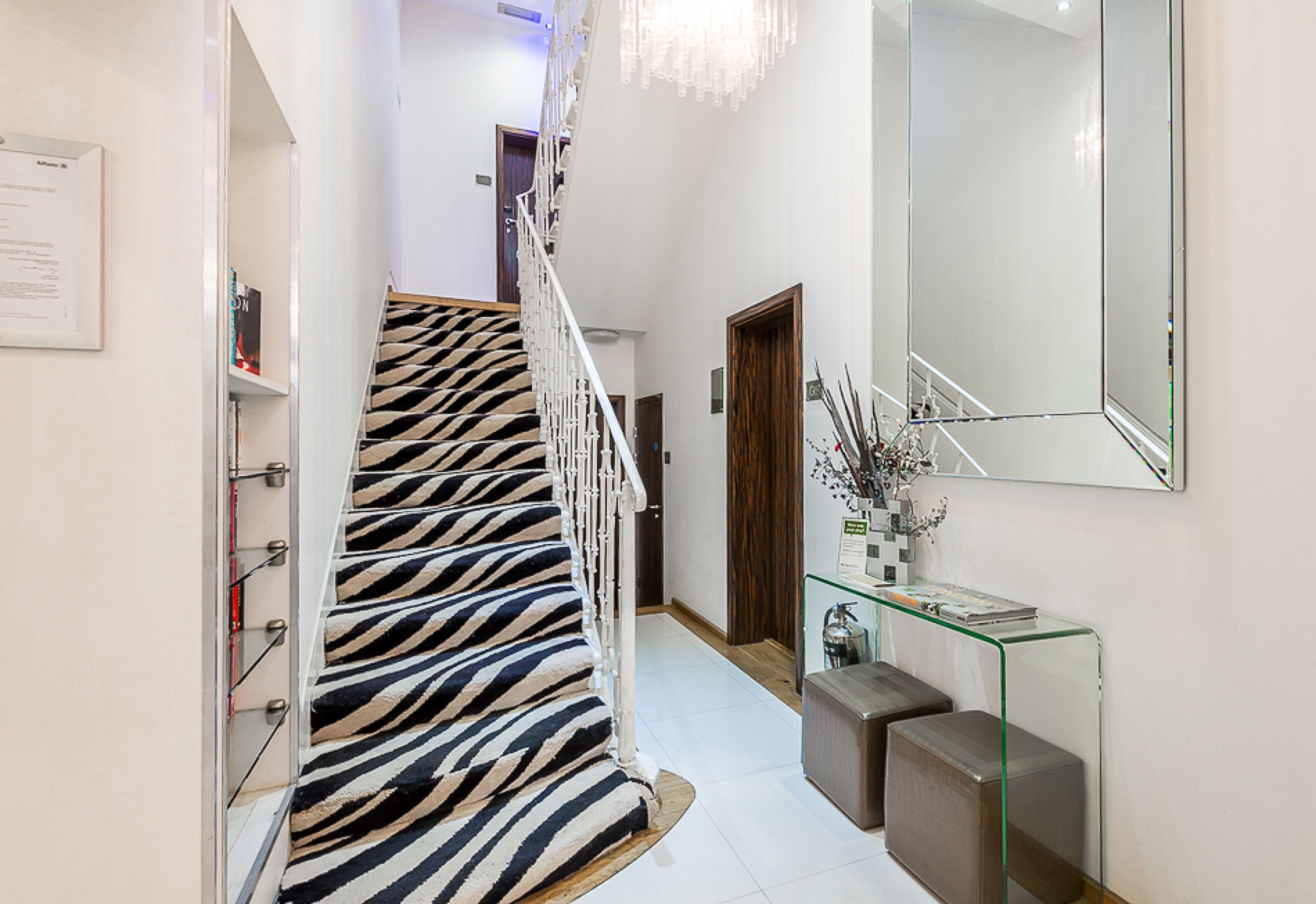 A staircase with zebra-striped carpet, a glass console table with decorative items, and a large mirror on the wall.