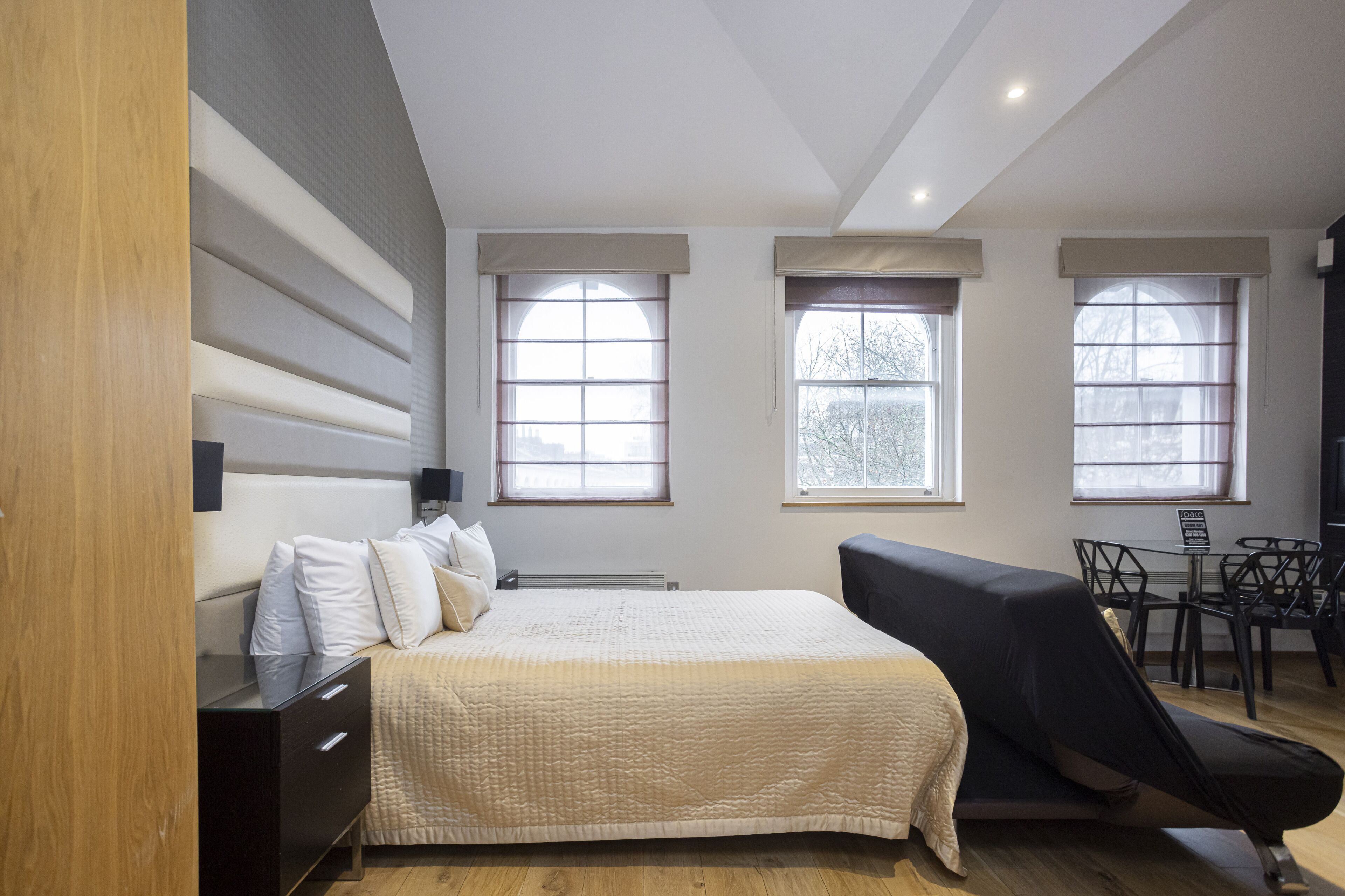 A modern bedroom with a bed, bedside table, and a desk with chairs.