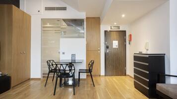A modern living room with a wooden floor, a glass partition, a dining table with chairs, a sofa, and a cabinet.