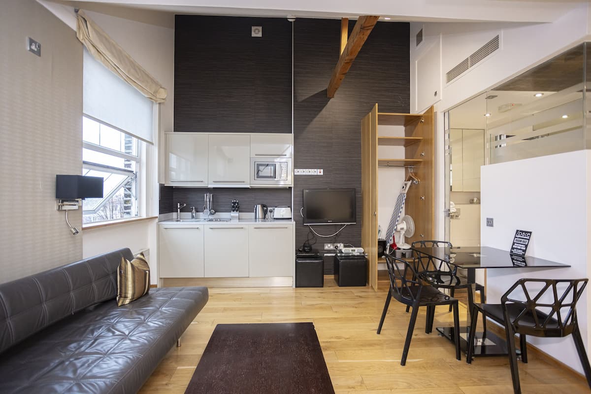 A modern living room with a sofa, a coffee table, a TV, and a dining area with chairs and a table.