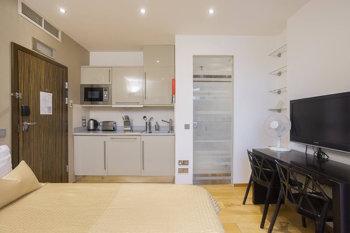 A hotel room with a bed, a desk with a TV, a kitchenette, and a walk-in closet.