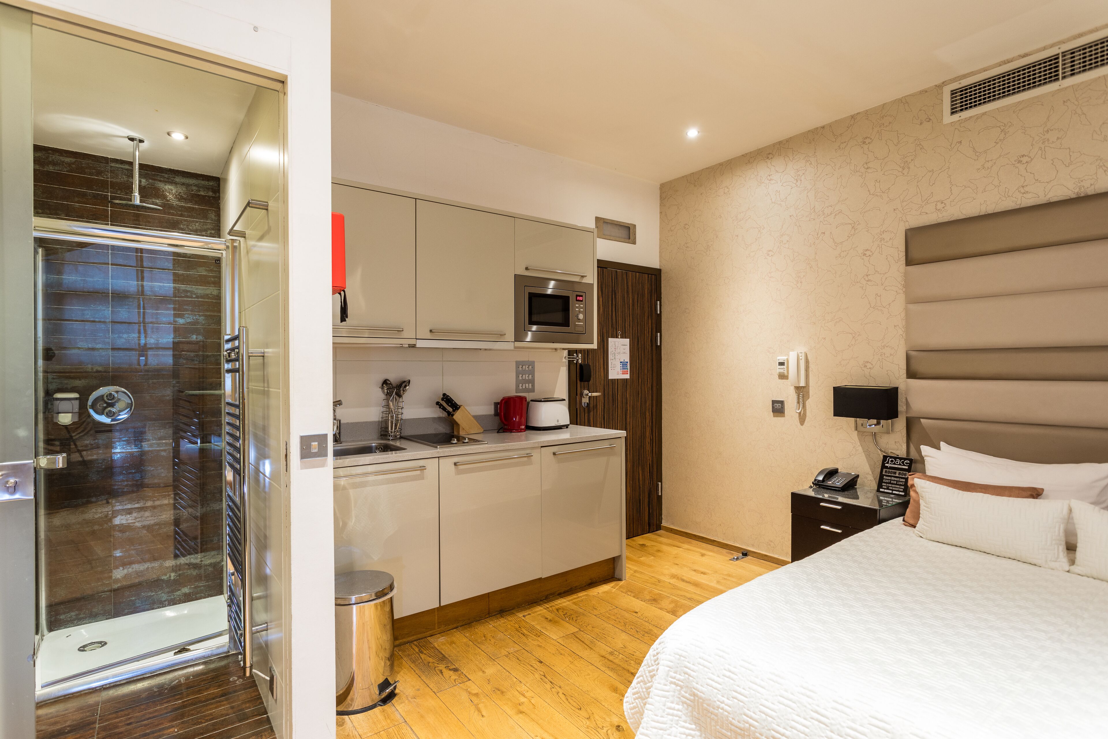Une chambre d’hôtel de taille réduite, dotée d’une douche, d’une kitchenette et d’un lit.
