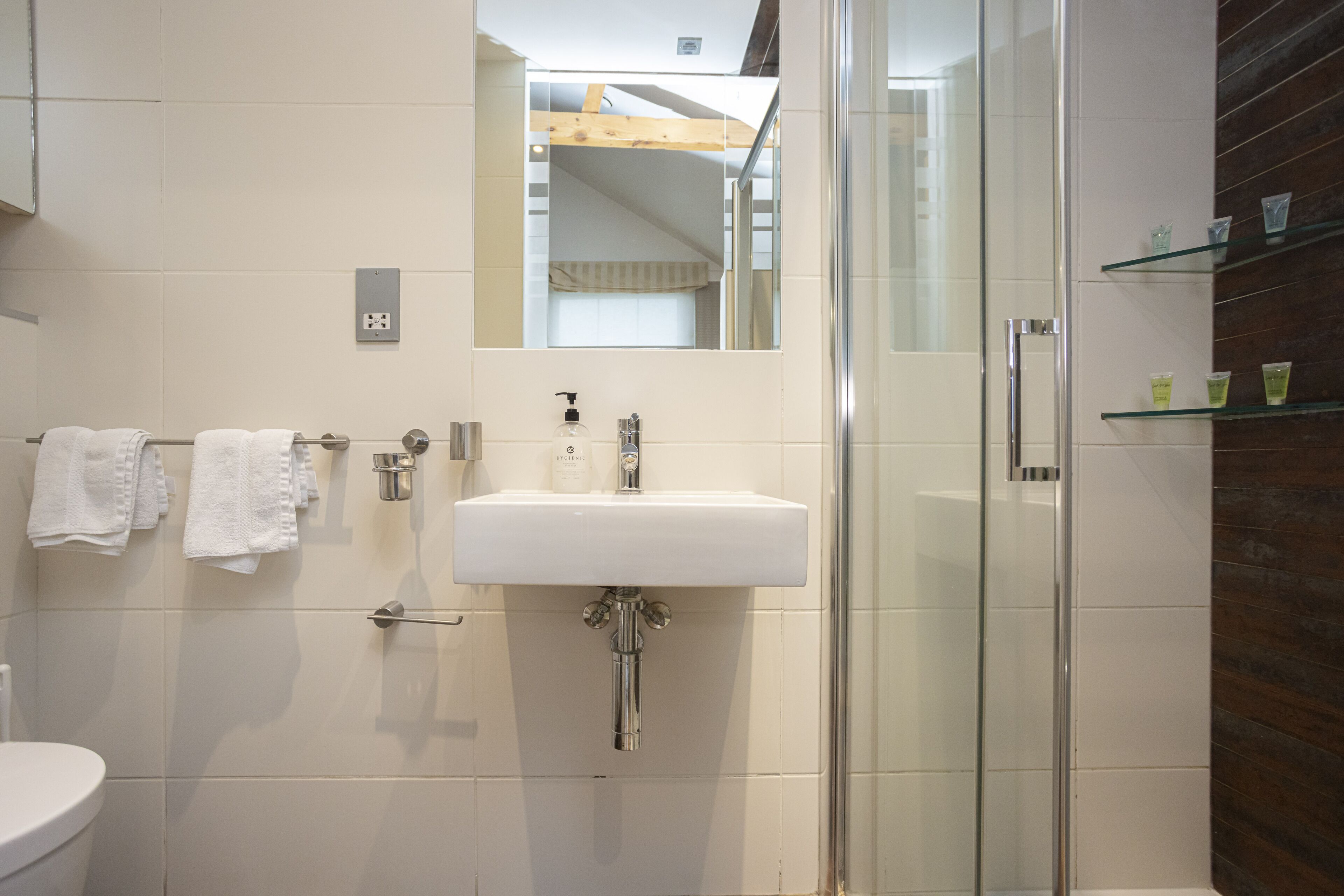 A modern bathroom with a white sink, glass shower enclosure, and a wooden ceiling.