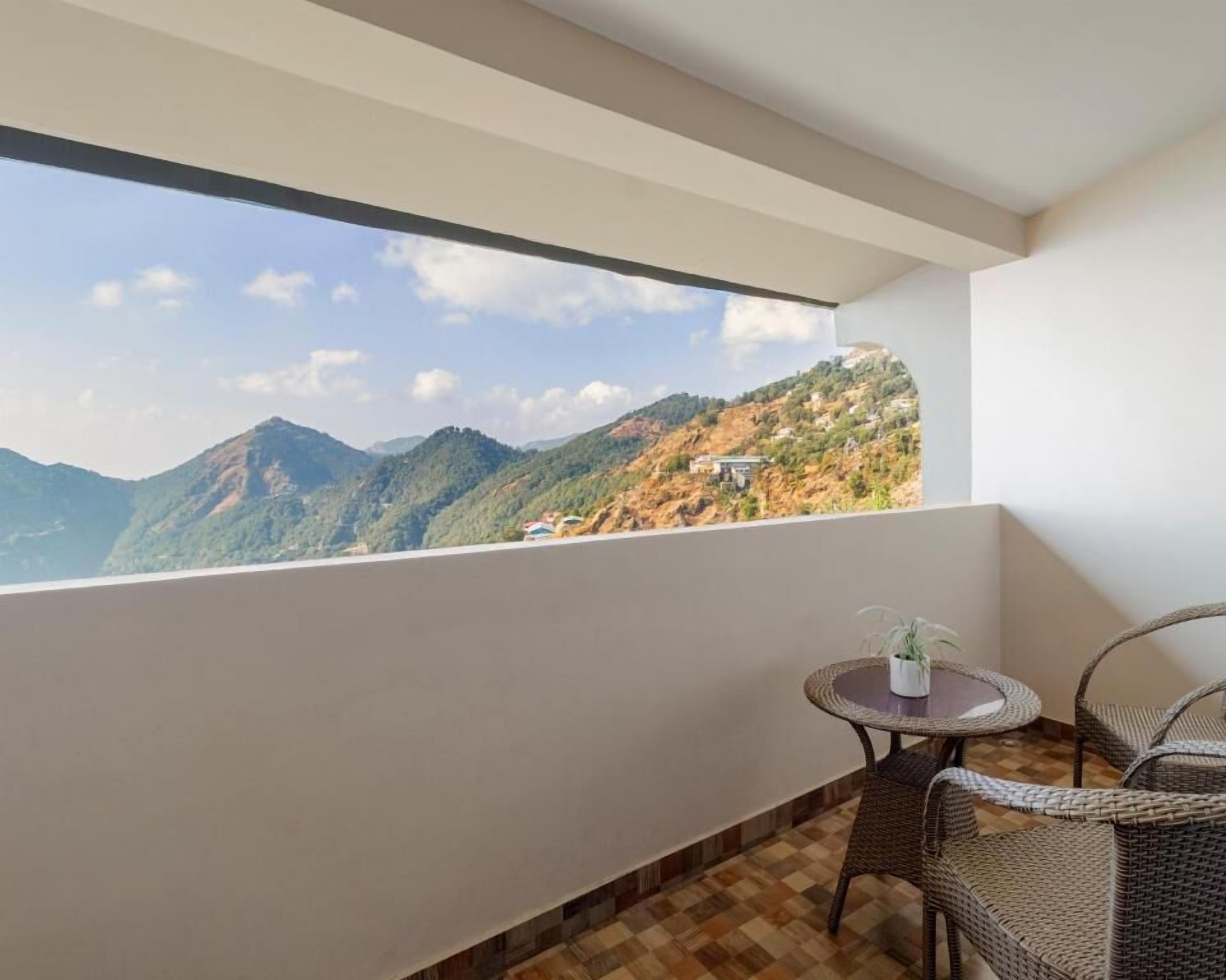 A balcony with a view of mountains, a wicker chair, and a small table with a plant.