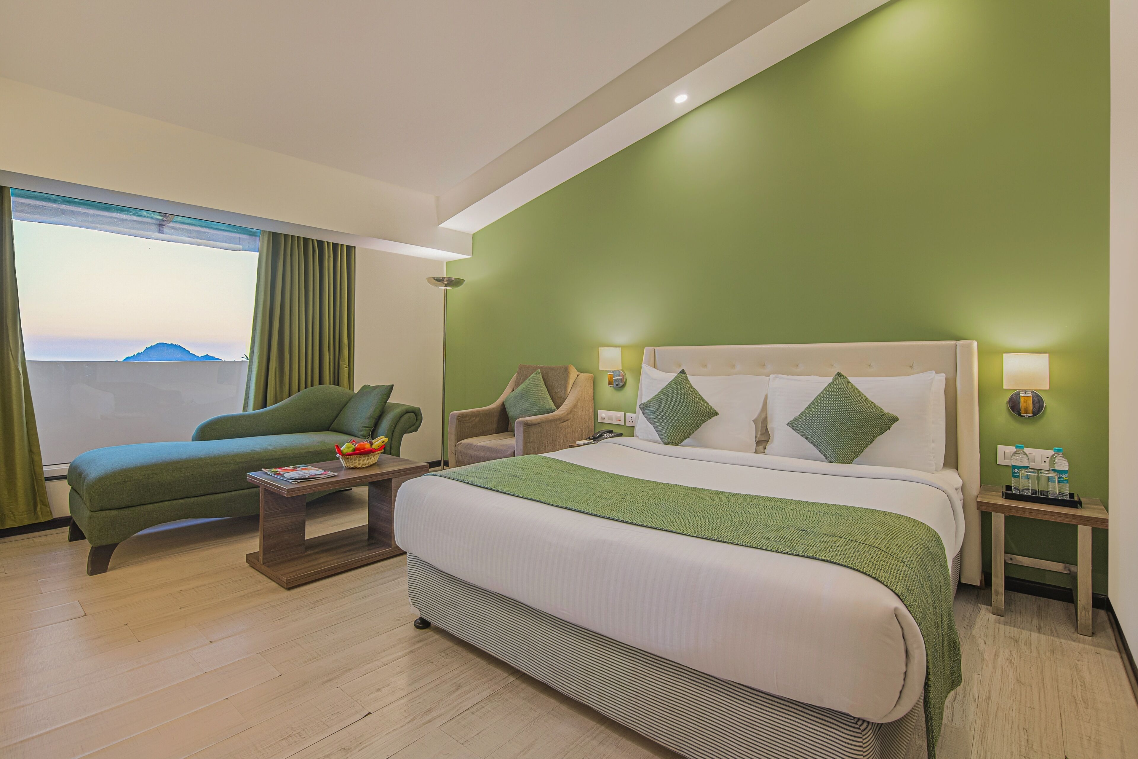 A hotel room with a bed, two armchairs, a small table, and a view of the outdoors.