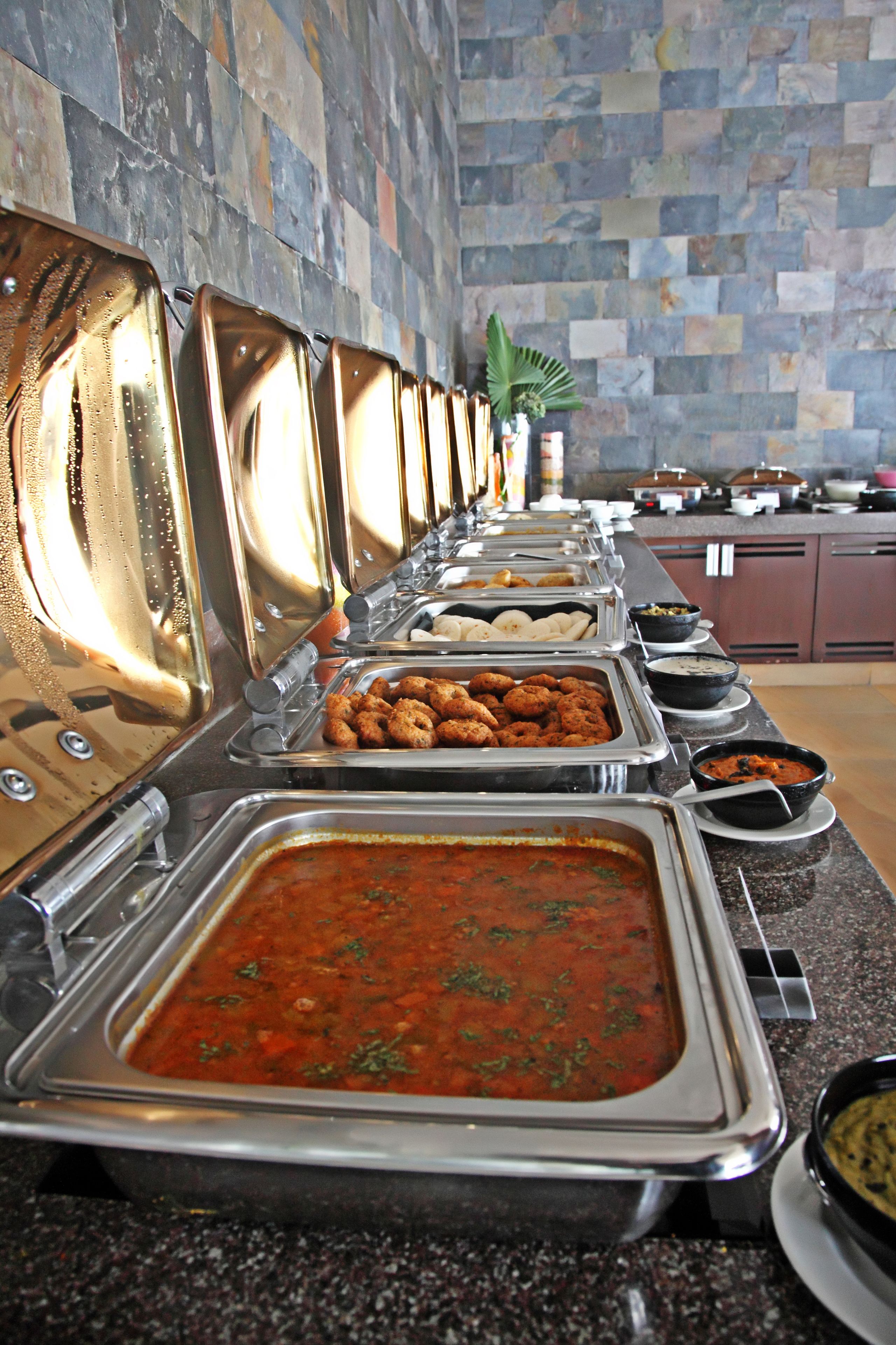 Una barra de buffet con diversas opciones de comida, incluyendo un recipiente grande de sopa y varias bandejas de aperitivos.
