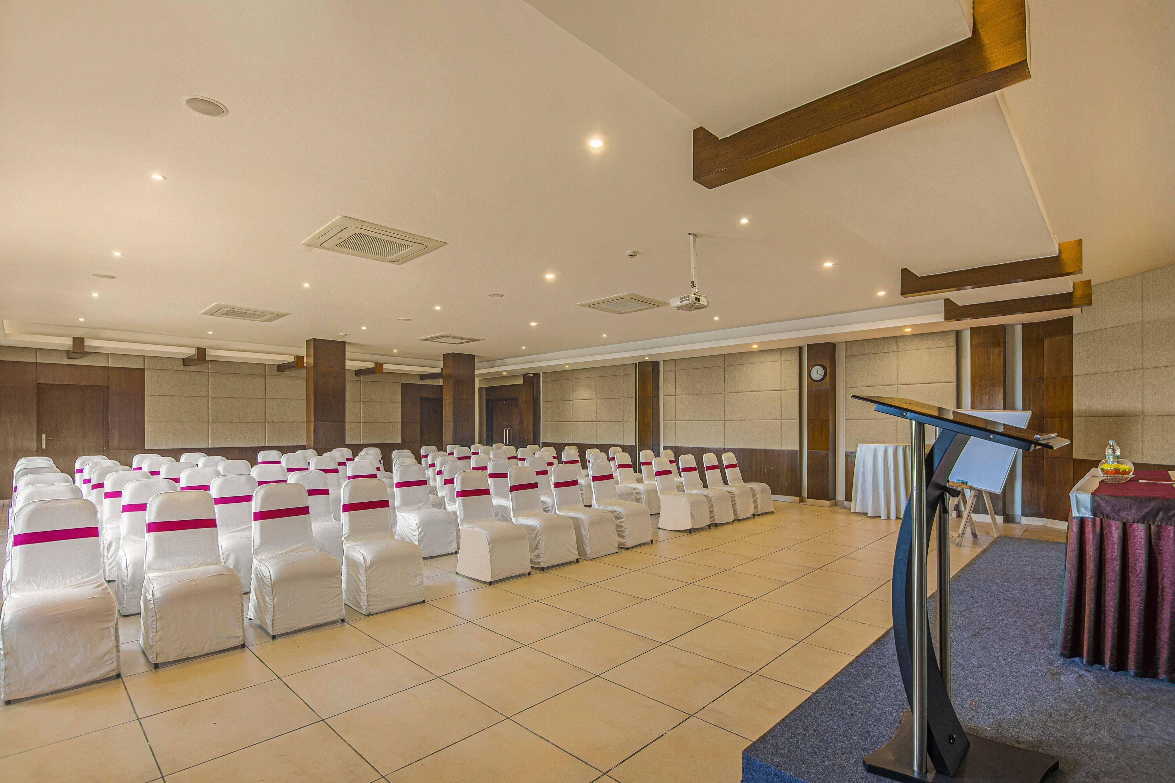 A conference room with rows of white chairs with pink sashes, a podium, and a clock on the wall.