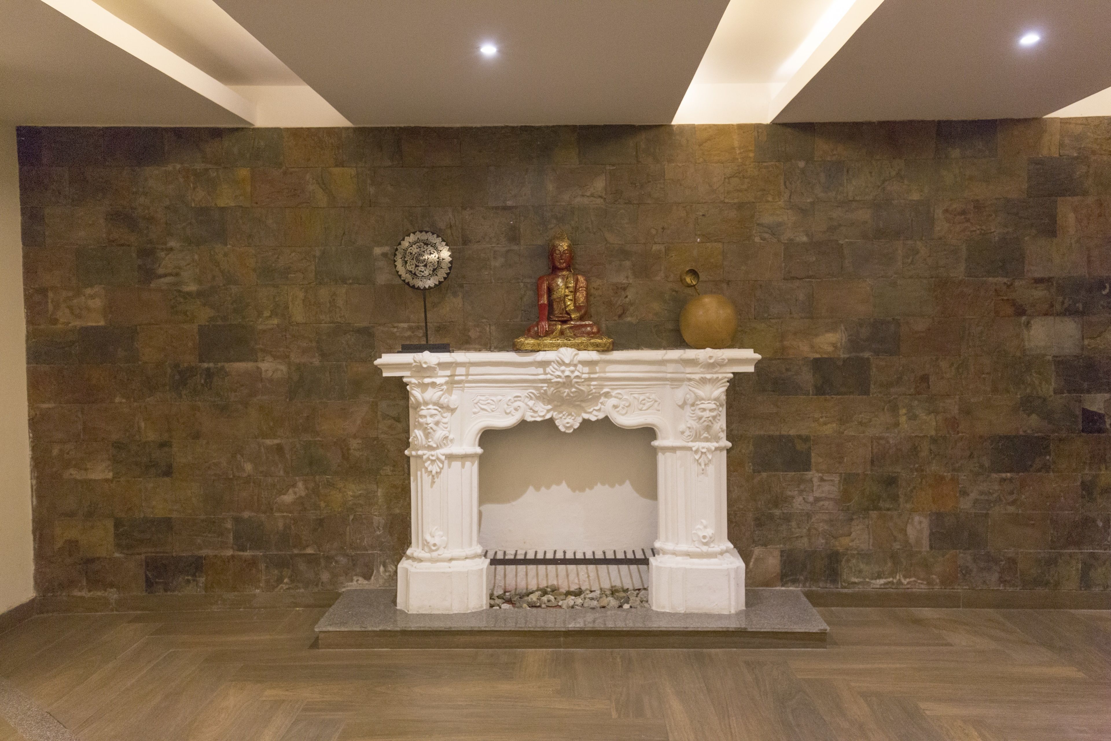 A room with a stone wall, a white fireplace with a Buddha statue, and a decorative vase.