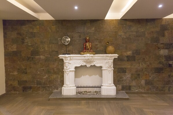 A room with a stone wall, a white fireplace with a Buddha statue, and a decorative vase.