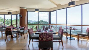 Un restaurante con amplios ventanales que ofrecen vistas a las montañas. Las mesas están dispuestas con sillas y centros de mesa.