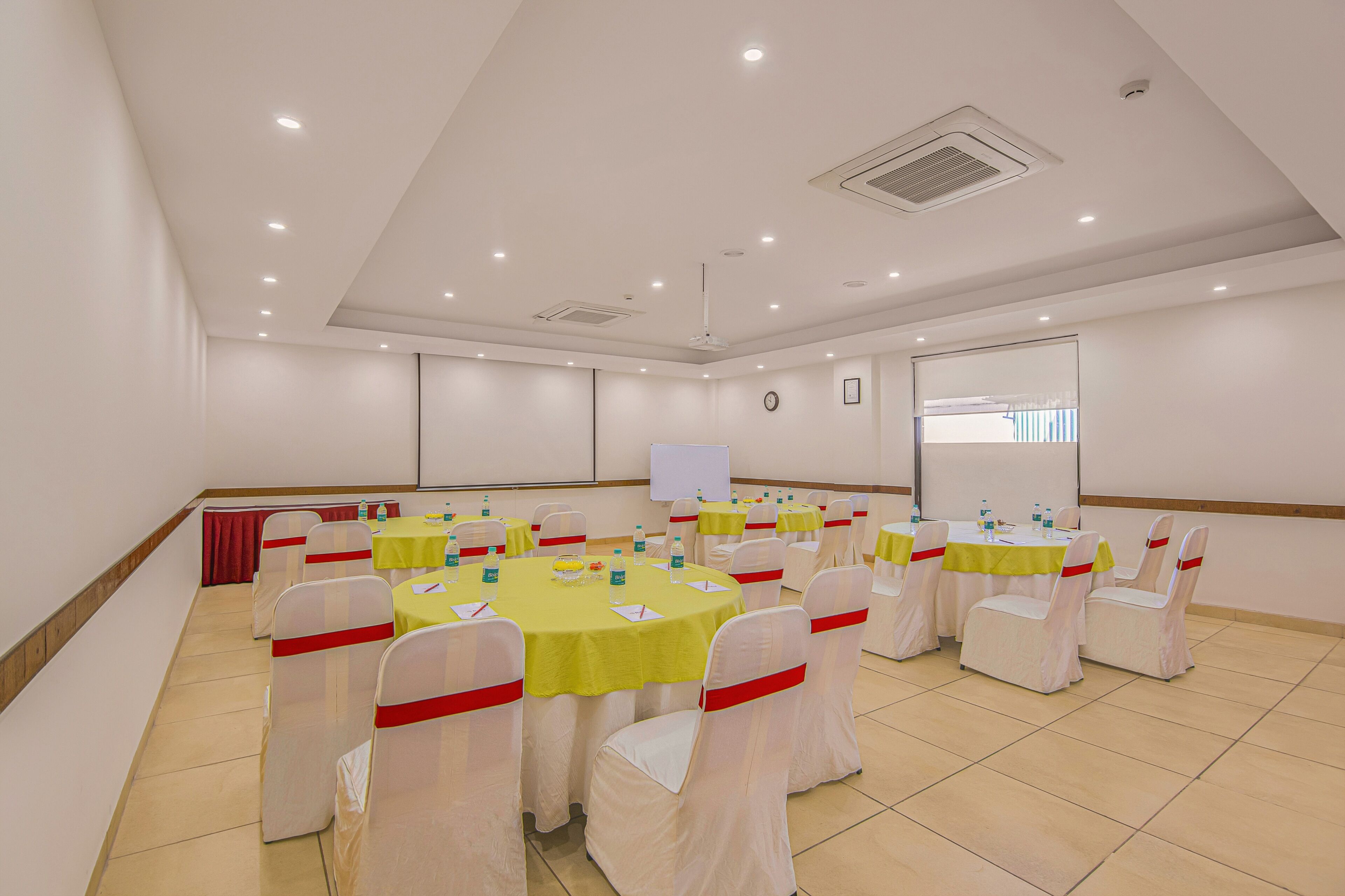 A conference room with round tables, white chairs with red sashes, and a projector screen.