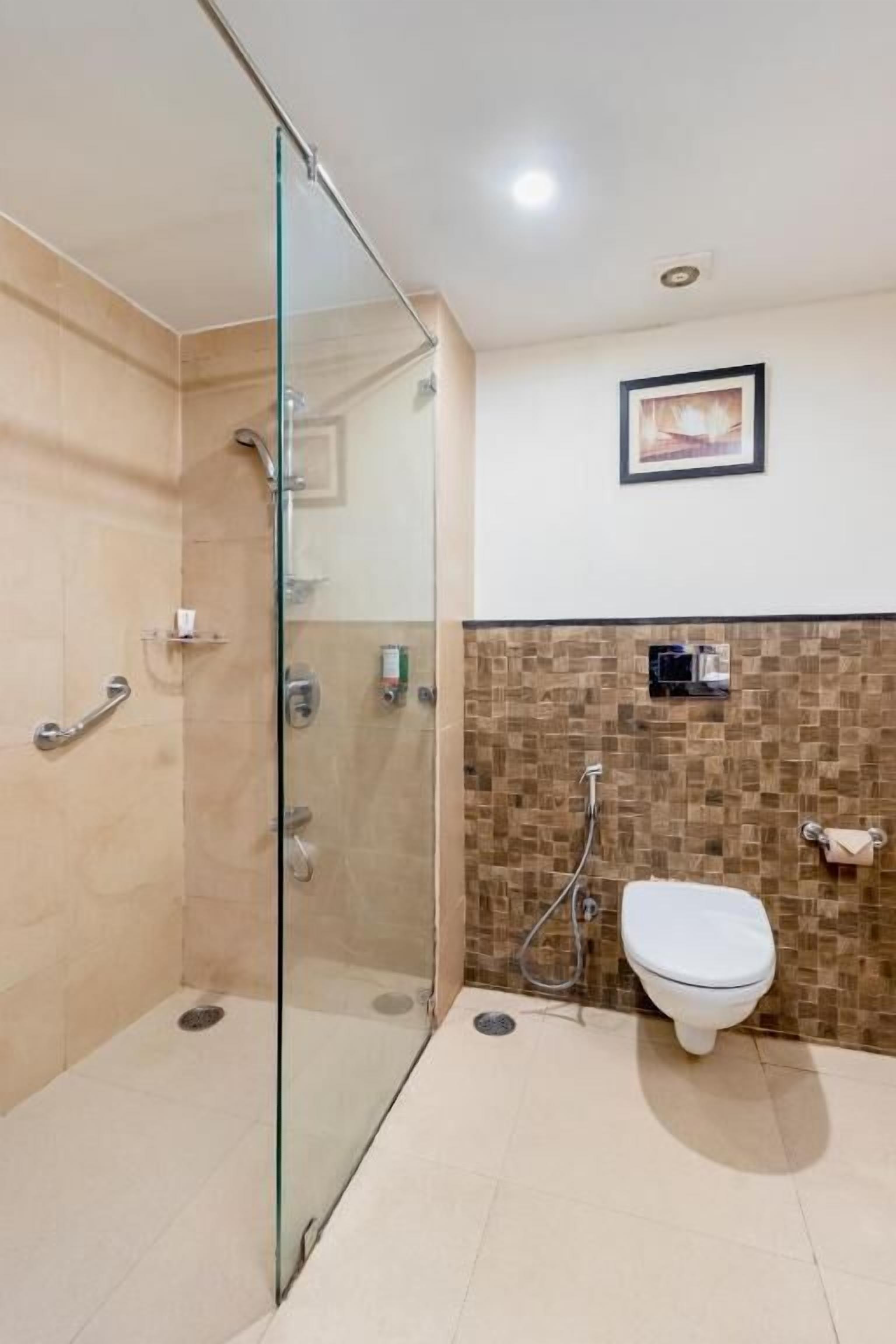 A bathroom with a glass shower enclosure, a toilet, and a tiled wall with a picture frame.
