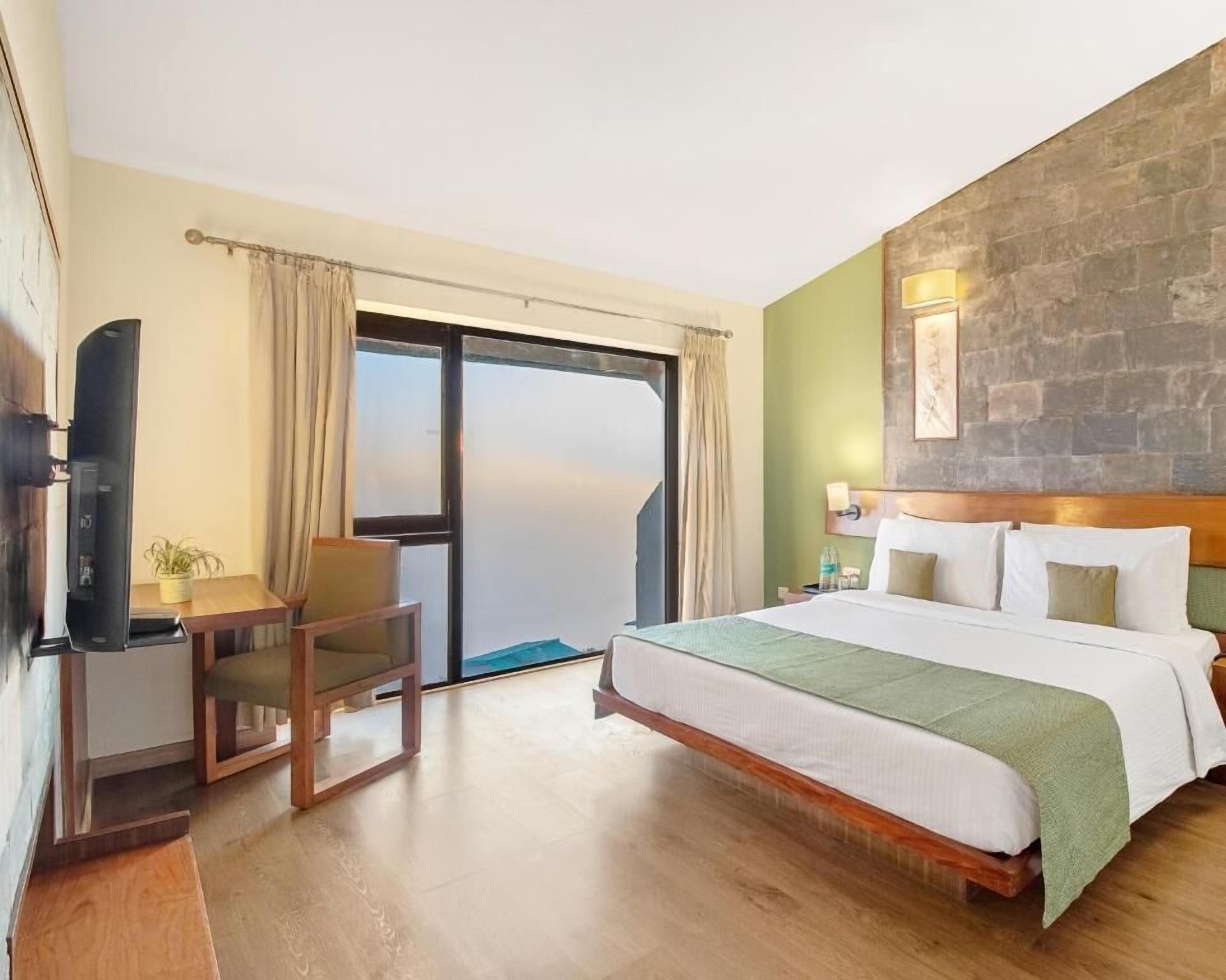 A hotel room with a bed, a desk, a chair, a television, and a large window.