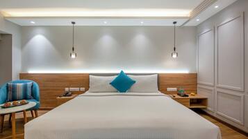 Une chambre d’hôtel moderne avec un grand lit, une table de chevet avec une lampe, une chaise et une petite table sur laquelle sont disposés des fruits.