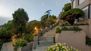 Una escalera con peldaños que suben hacia un edificio, rodeado de follaje y flores.