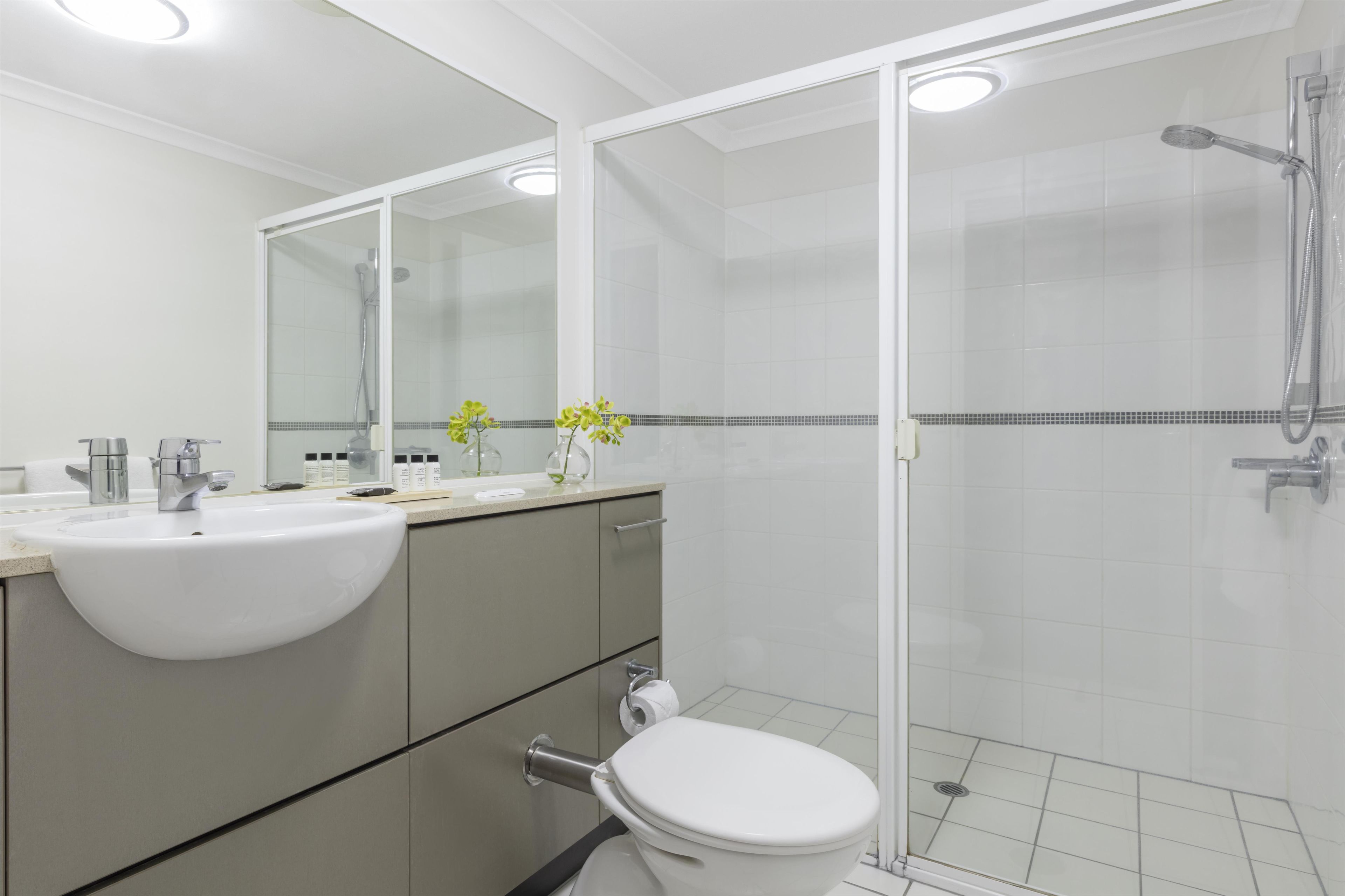 Un baño moderno con lavamanos, espejo, inodoro y ducha blancos.