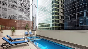 Un espace piscine aménagé sur le toit, avec des chaises longues et une piscine.