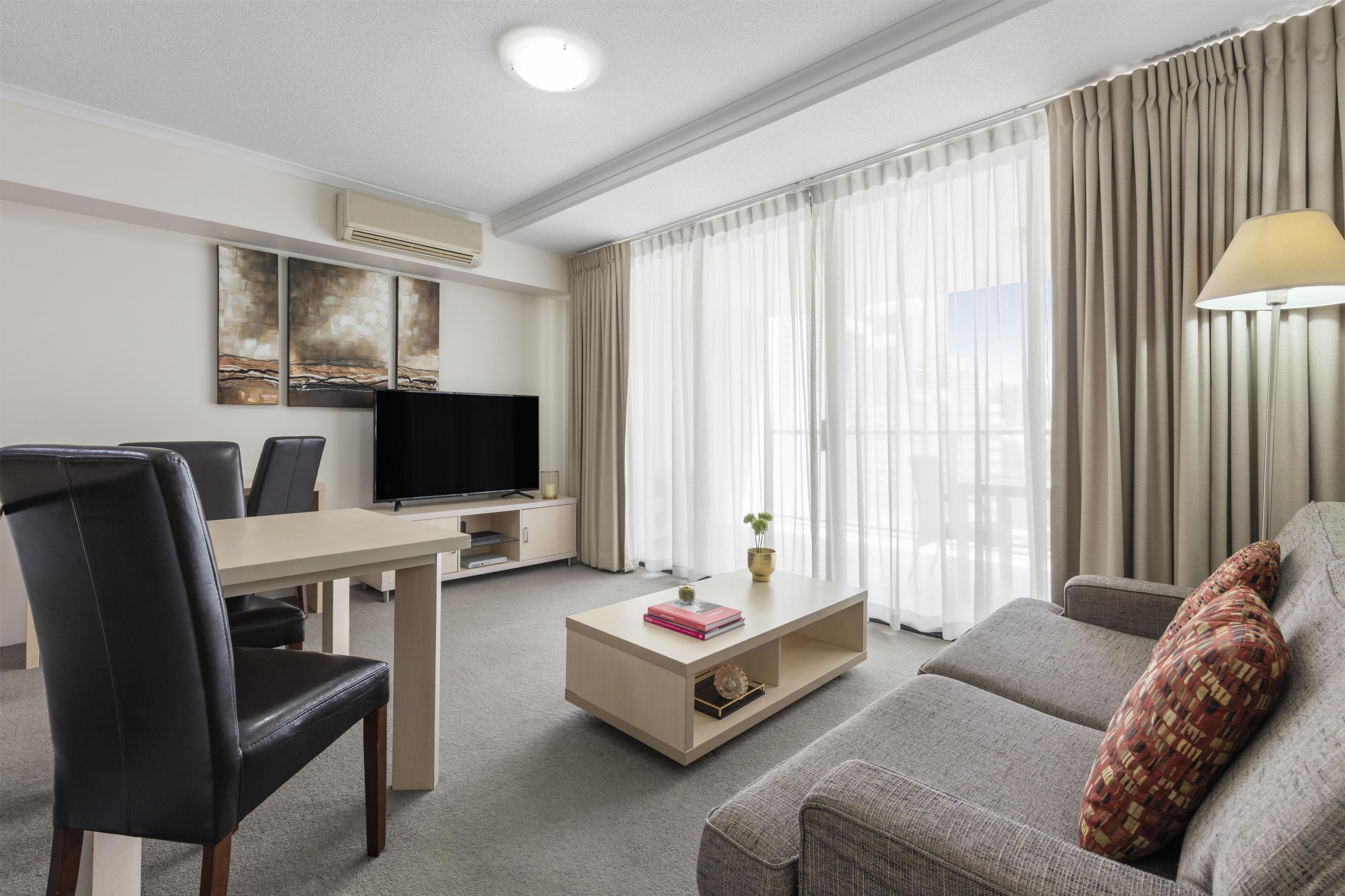 Quarto de hotel moderno com TV de tela plana, mesa de jantar, sofá e mesa de centro.